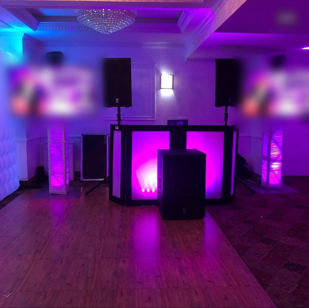 A white-scrim DJ facade lit magenta, flanked by two vertical screens on truss towers.